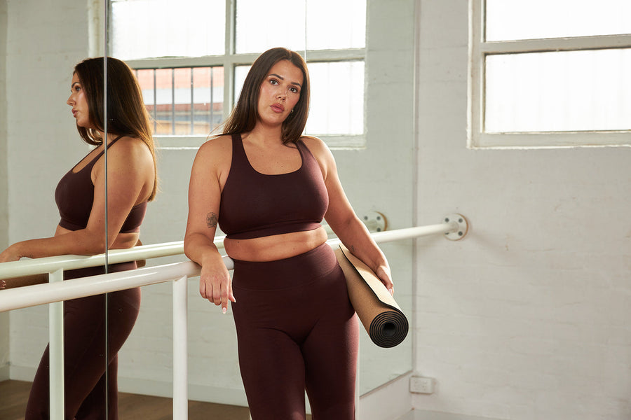Woman training with a dumbbell in a merino sports bra and leggings in a studio