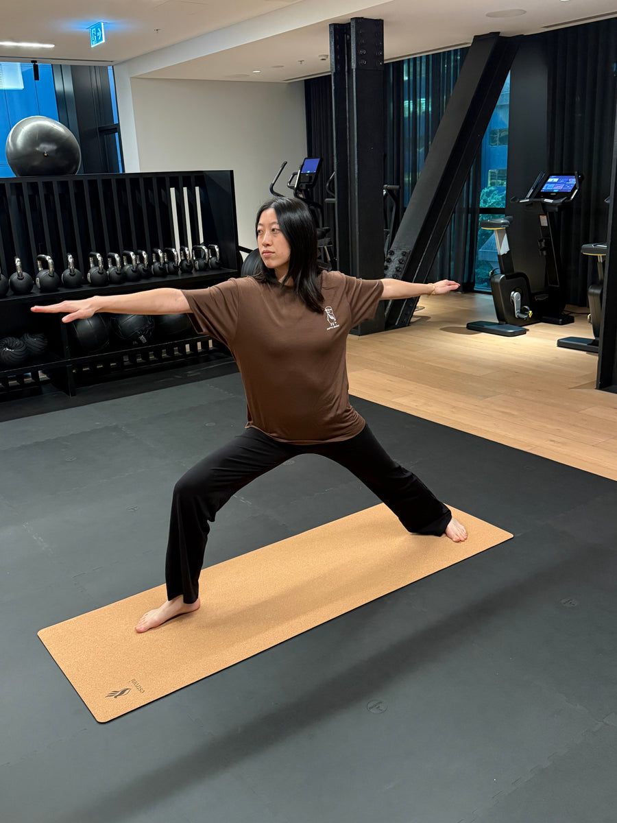 Woman in warrior pose on a cork yoga mat wearing merino activewear